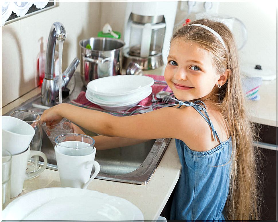 Little girl with great childish independence washing her dishes after eating.