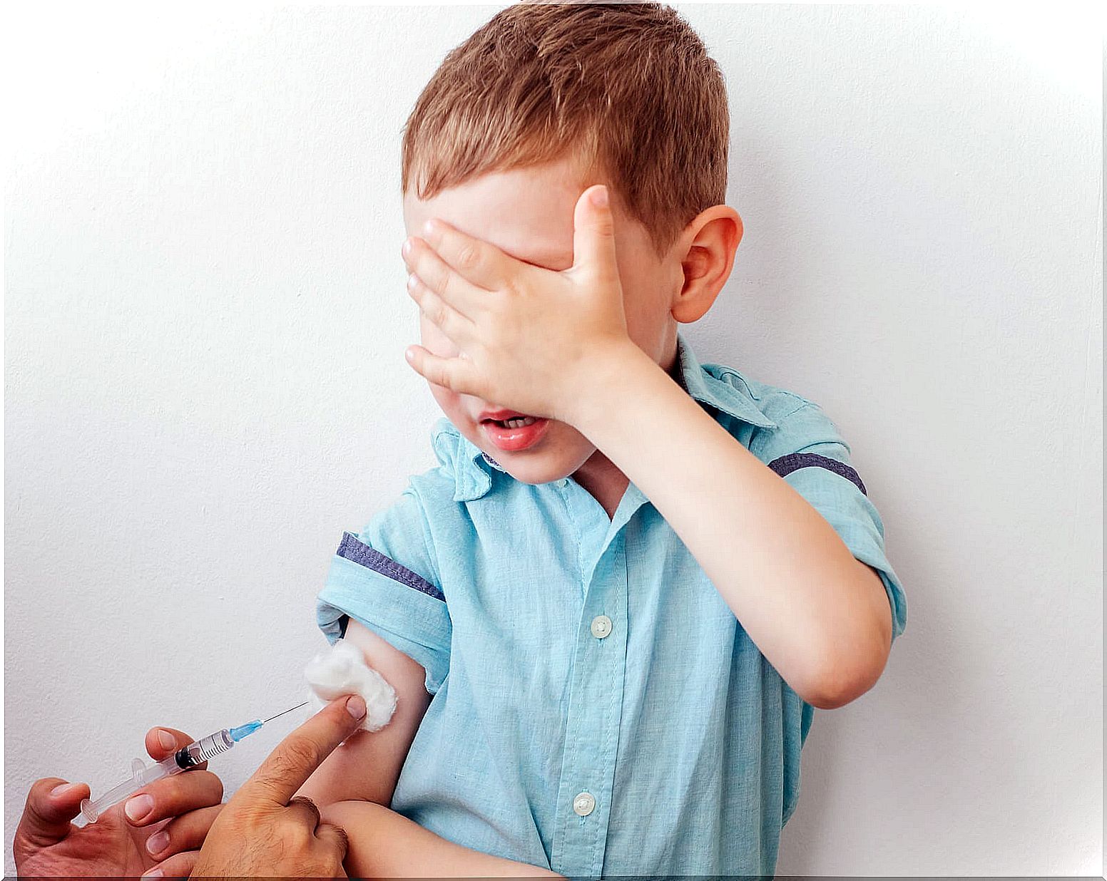 Child at the pediatrician covering his face because he is afraid while being vaccinated.