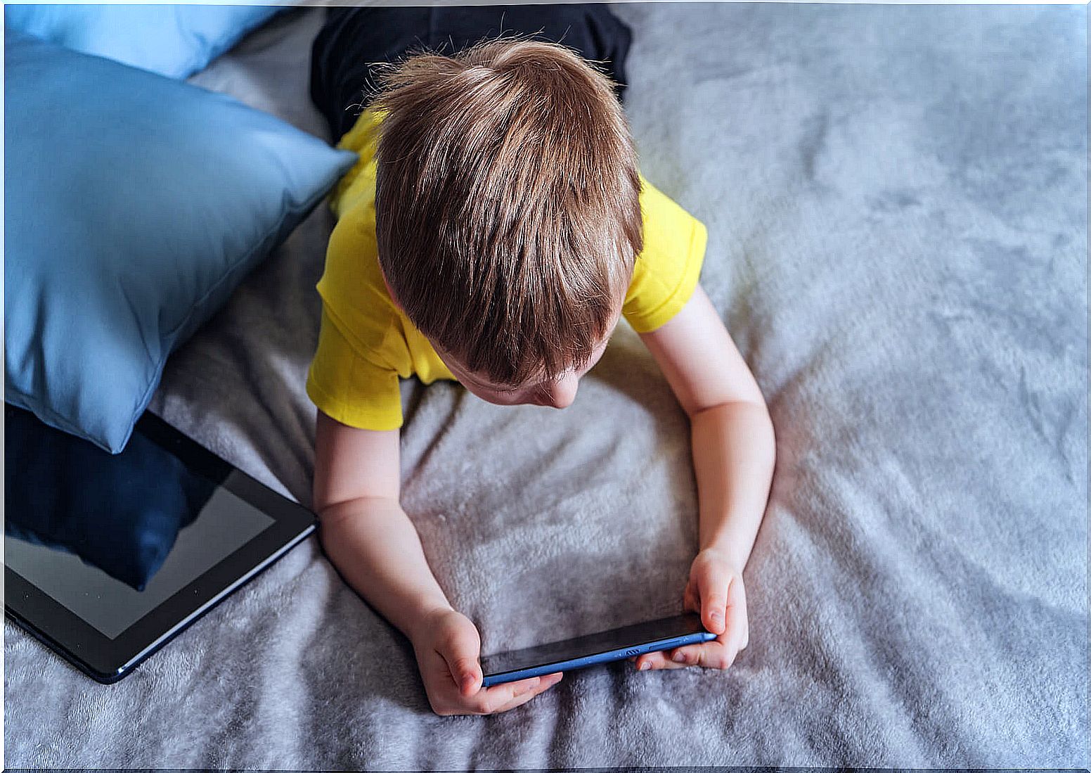 Child with a tablet by the side while playing with the mobile with the child syndrome.