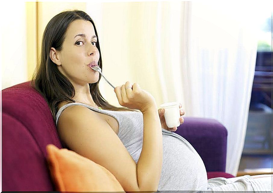 Happy pregnant woman at home eating white yogurt